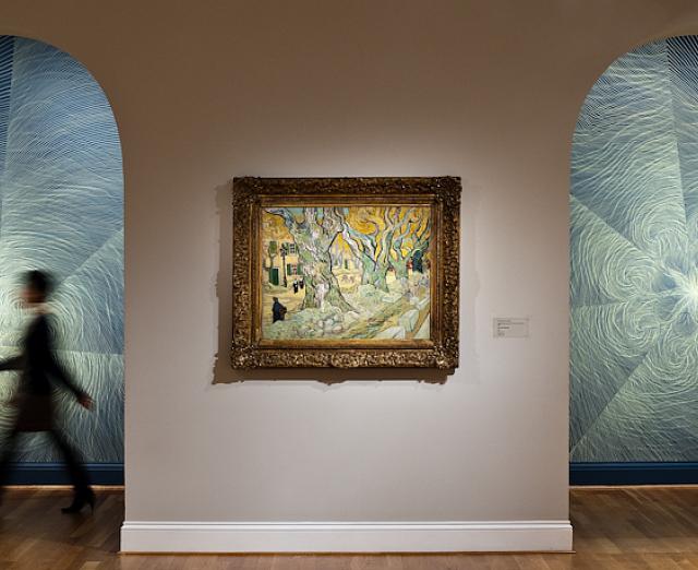 Photo of a figure walking in front of walls with drawings by linn meyers, with a painting by Van Gogh on display 